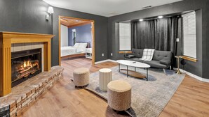 A modern living room with a fireplace, a sofa, a coffee table, and a bed in the background. - NEW - Fire pit - Game room - Sleeps 14 - 40 acres (Ahwahnee)