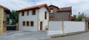 Ein zweistöckiges Haus mit weißer Fassade, einer Steinwand auf der rechten Seite und einem roten Ziegeldach.