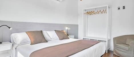 Quarto moderno com cama, mesas de cabeceira, luminária pendente, guarda-roupa e uma cadeira.