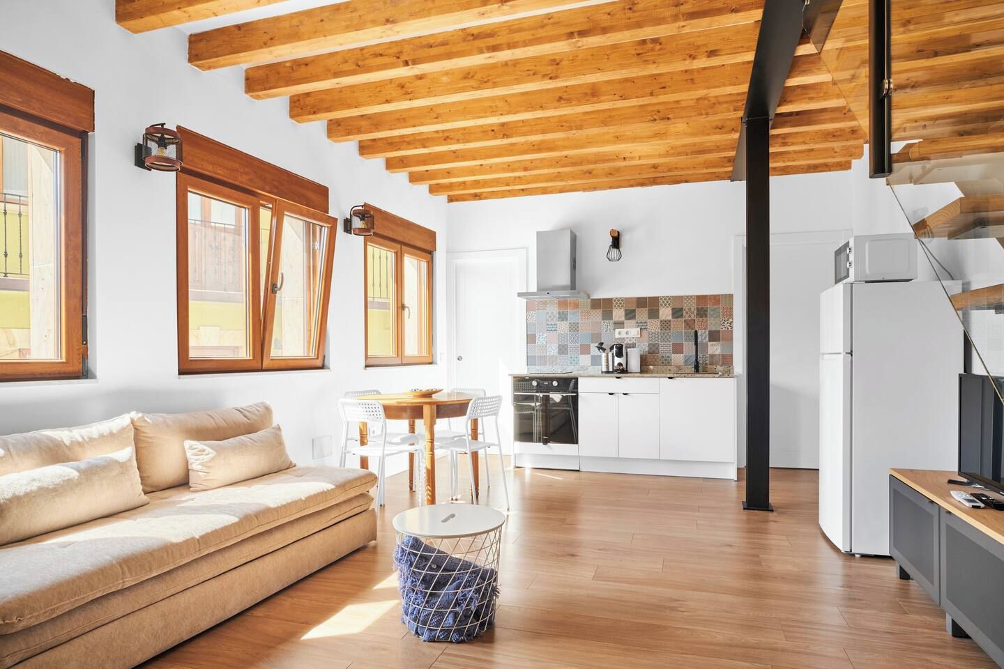 A modern interior with a wooden ceiling, a kitchen area with white cabinets, and a seating area with a sofa and chairs.