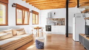 Un interior moderno con techo de madera, una zona de cocina con armarios blancos y un espacio de estar con sofá y sillones.