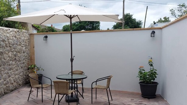 Un patio con una mesa redonda y cuatro sillas, un paraguas grande y plantas en macetas.