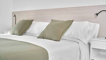 Una cama bien hecha con ropa de cama blanca y verde, una lámpara de noche y una mesita de noche blanca.