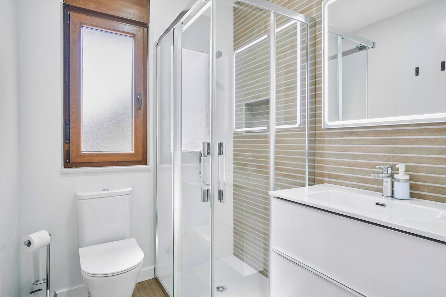 Un baño moderno con cabina de ducha de vidrio, inodoro blanco y tocador con espejo.