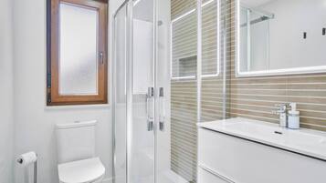 Un baño moderno con cabina de ducha de vidrio, inodoro blanco y tocador con espejo.