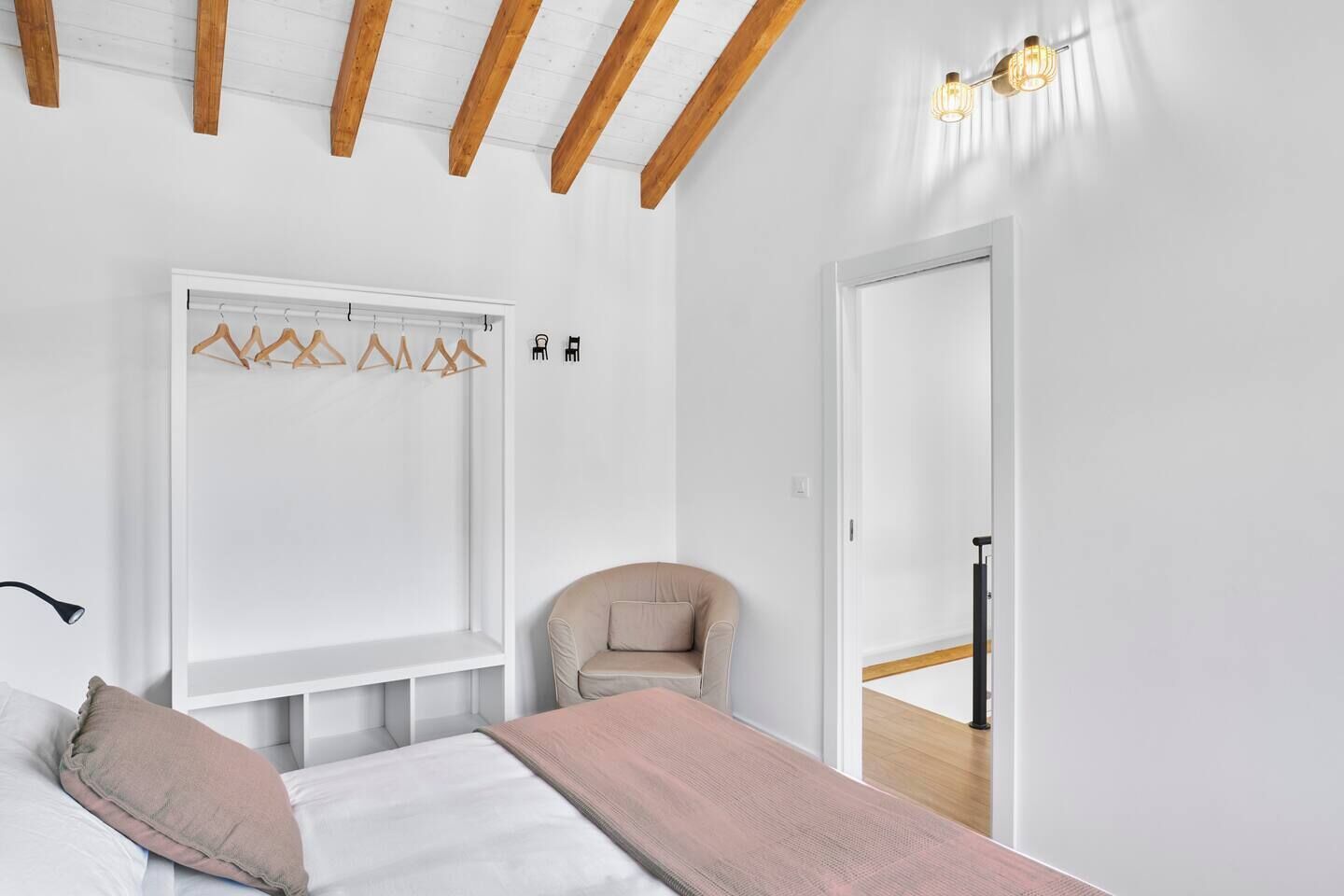 Een slaapkamer met een bed, een stoel, een kapstok en een deur naar een andere kamer.
