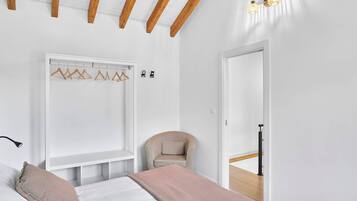 Een slaapkamer met een bed, een stoel, een kapstok en een deur naar een andere kamer.
