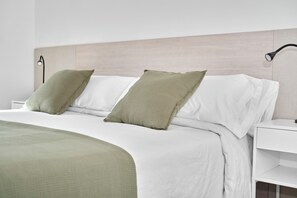 Ein ordentlich bezogenes Bett mit weißer und grüner Bettwäsche, ein moderner Kopfteil und ein Nachttisch mit einer Lampe.