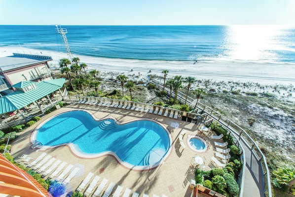 A resort with a large swimming pool, sun loungers, and a view of the beach and ocean.
