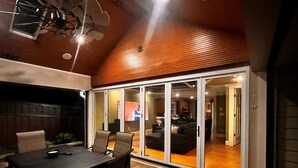 Un patio al aire libre con una mesa y sillas de comedor, techo de madera y una puerta corrediza de vidrio que da a un salón interior.