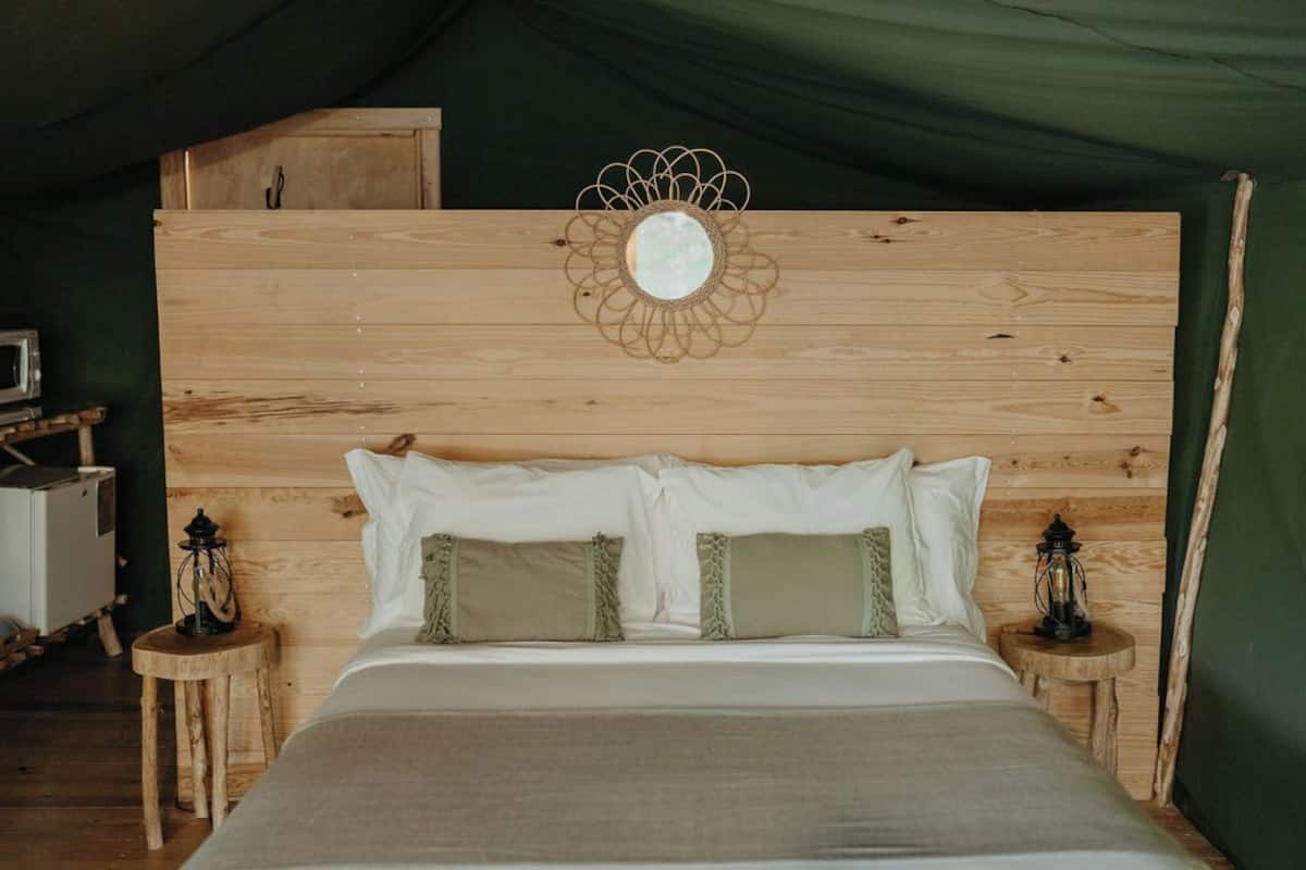 Un lit en bois avec des oreillers blancs et verts, un miroir sur la tête de lit et deux petites tables de chevet en bois avec des lanternes.