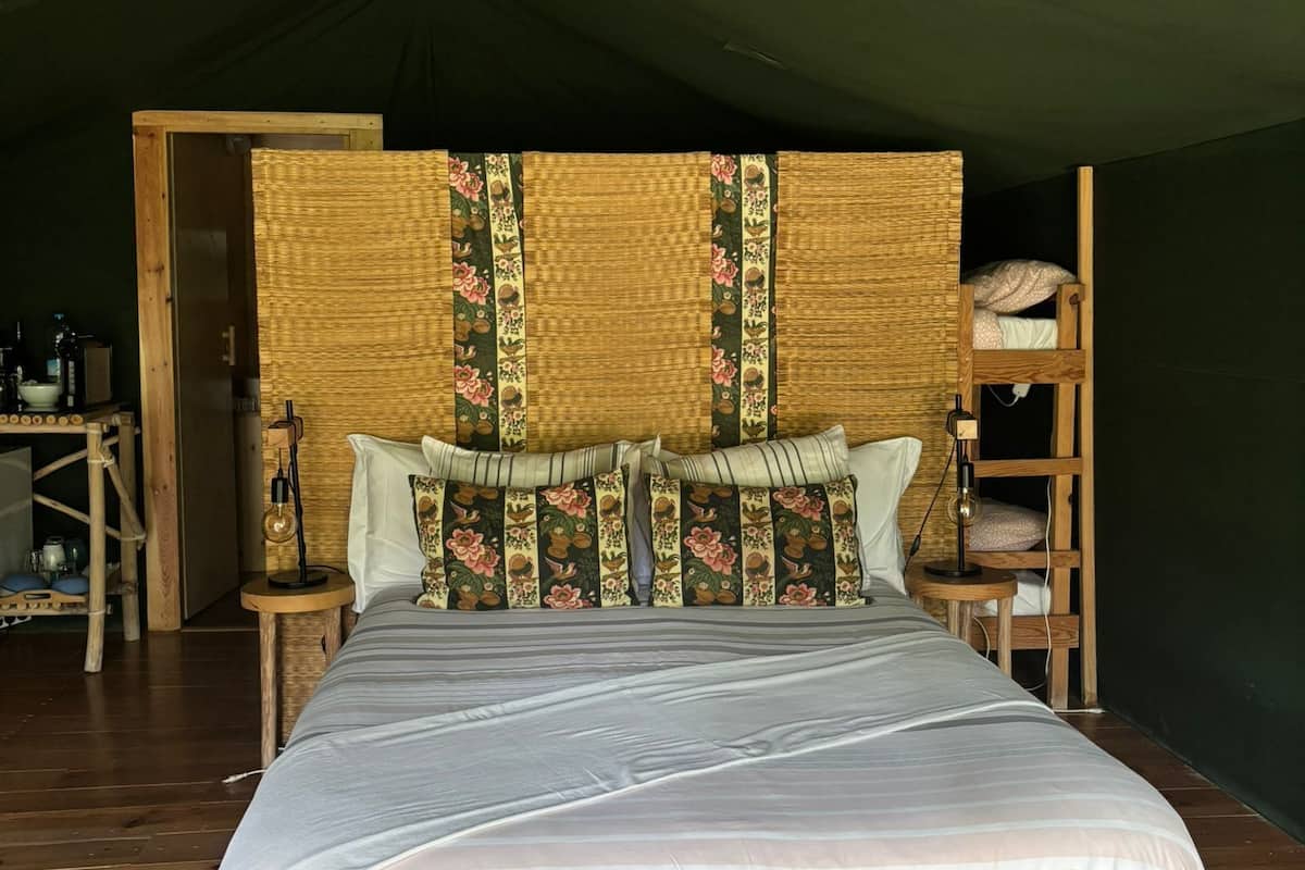 Une pièce aménagée comme une tente, avec un lit, des meubles en bois et une tête de lit en osier.