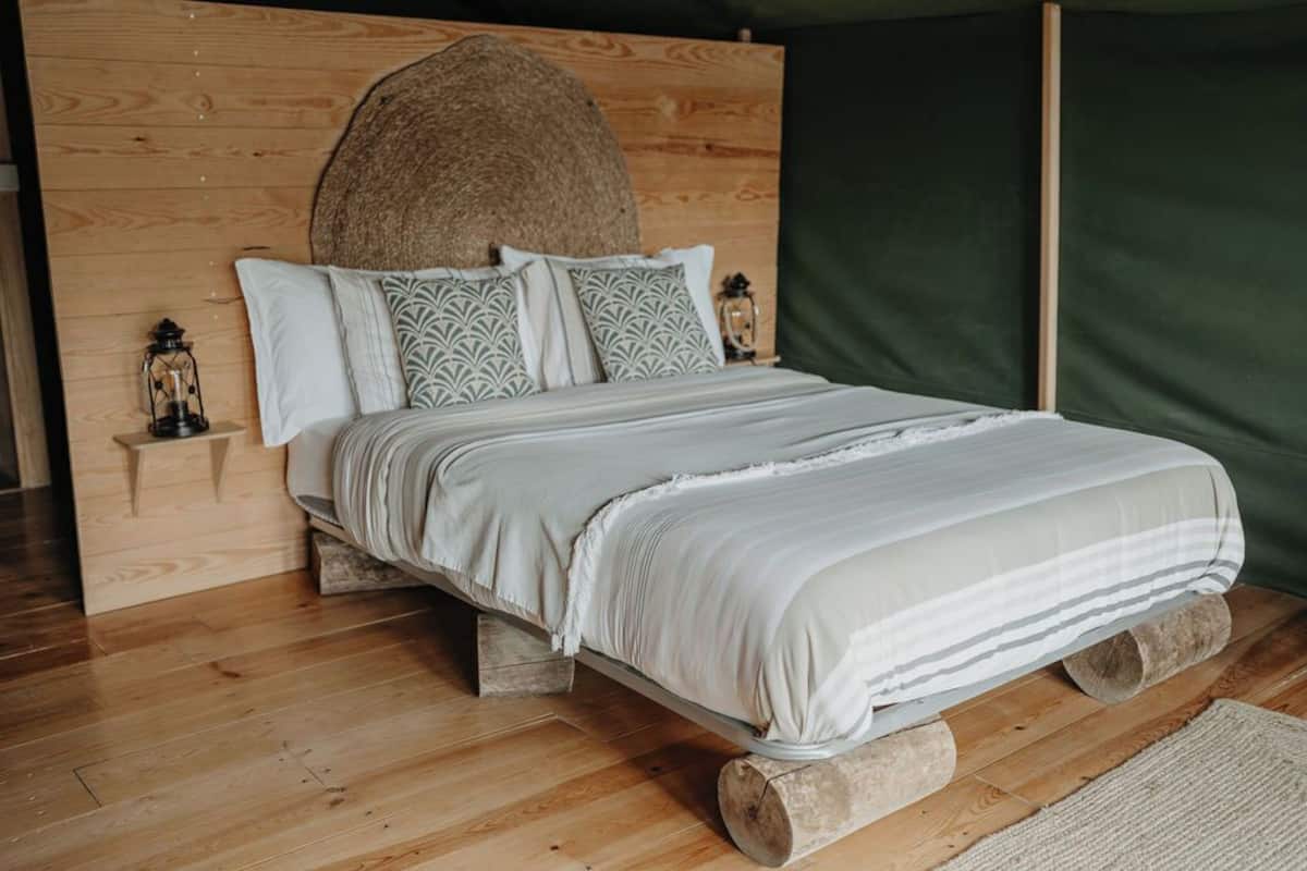 Un lit avec une tête de lit en bois, un coussin à motifs et une lanterne posée sur une table de chevet en bois.