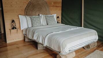 Ein Bett mit hölzernem Kopfteil, einem gemusterten Kopfkissen und einer Laterne auf einem Nachttisch aus Holz.