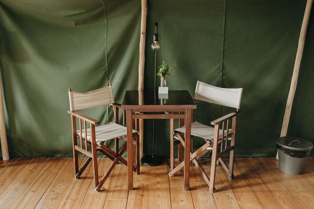 A wooden table with two chairs, a small potted plant, and a floor lamp in a room with green walls and wooden flooring.