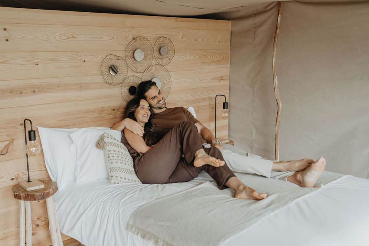 Une tête de lit en bois ornée de motifs circulaires, un lit avec du linge de lit blanc et deux lampes de chevet.