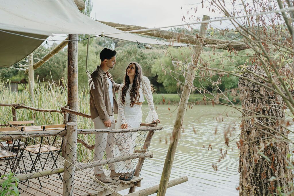 A couple standing on a wooden platform with a netted railing, overlooking a body of water.