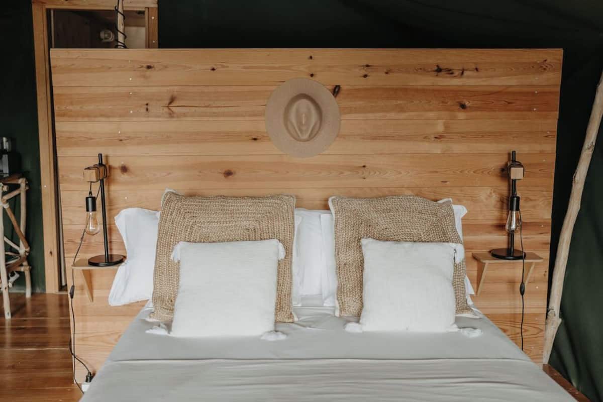 Une tête de lit en bois ornée d’un motif circulaire, deux lampes de chevet et un lit avec une literie blanche et deux coussins à texture particulière.