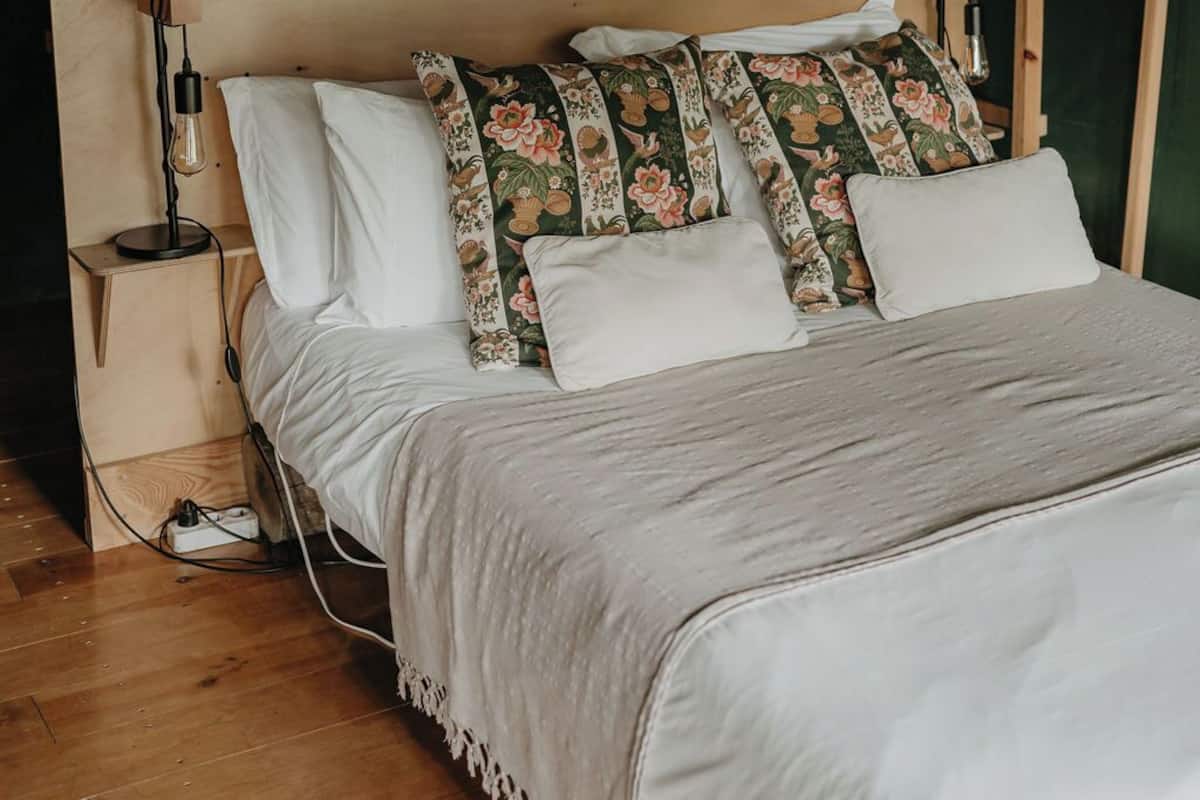 Un lit en bois avec une tête de lit en osier, une literie blanche et des coussins à motifs floraux.