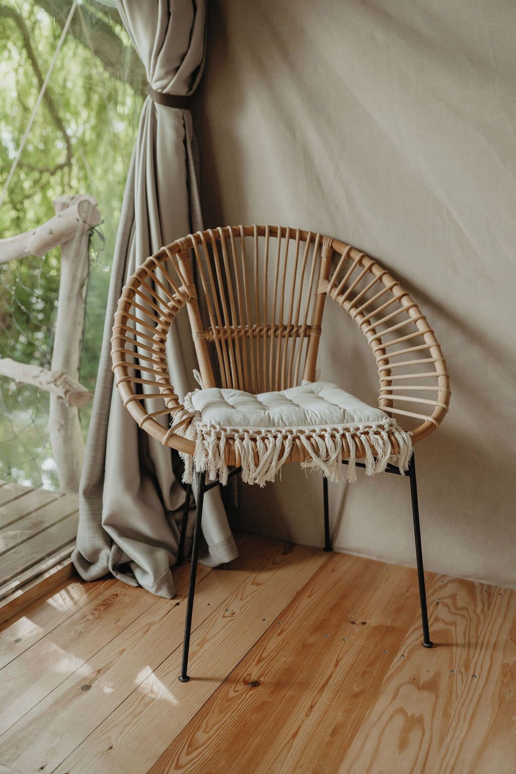 Una sedia in vimini con un cuscino, in una stanza con pavimento in legno e uno sfondo di tenda.