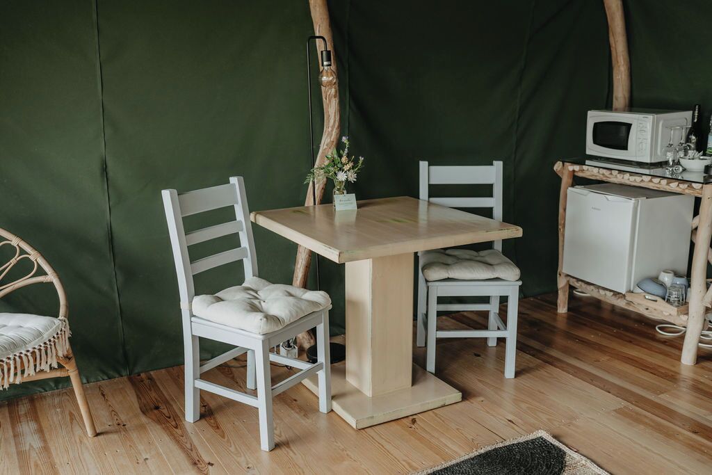 A cozy room with a wooden table and two white chairs, a small white cabinet with a microwave, and a wicker chair.