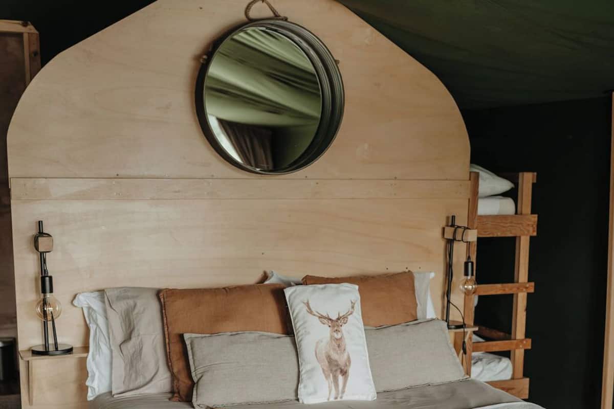 Un lit avec une tête de lit en bois, un miroir rond et plusieurs coussins, dont un orné d’un motif de cerf.