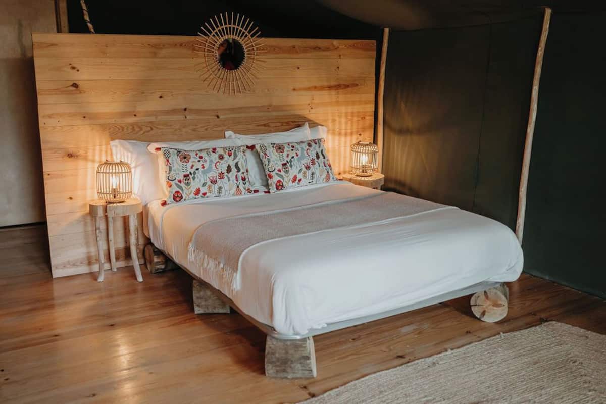 Un lit en bois avec une literie blanche, deux lampes de chevet et un élément décoratif mural.