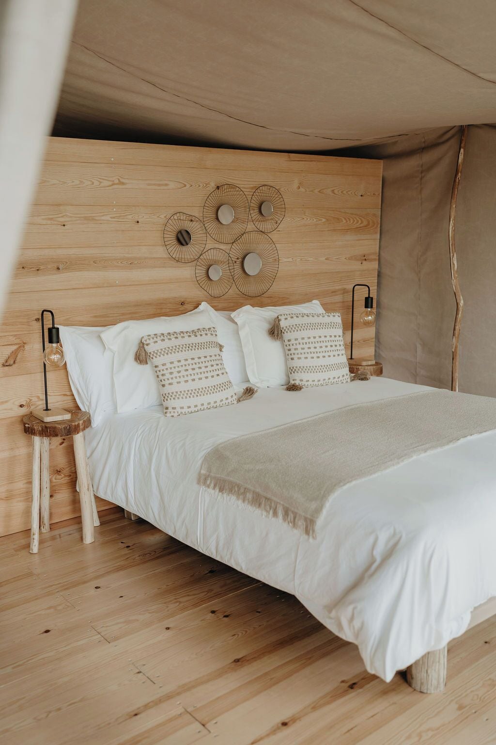 Een bed met een houten hoofdbord, witte beddengoed en gestreepte kussens. Twee nachtkastjes met lampen staan ernaast.