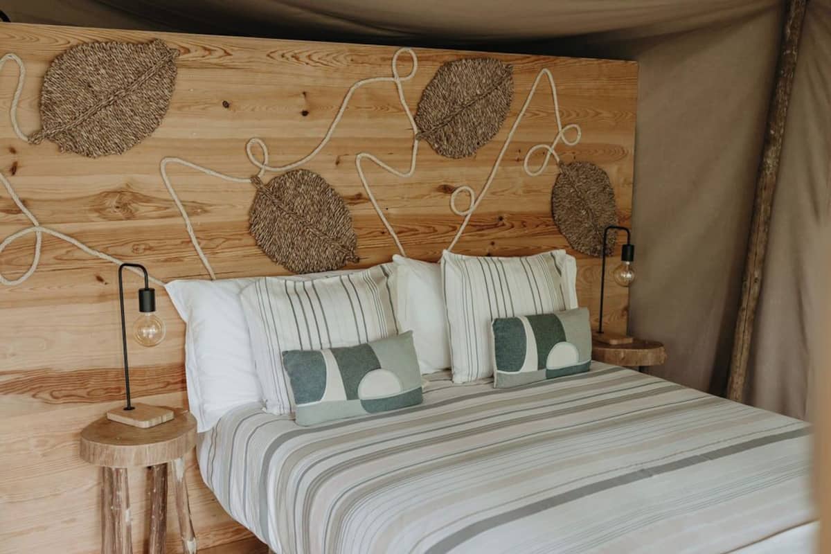 Un lit avec une literie à rayures, deux oreillers, une tête de lit en bois ornée de motifs végétaux tissés et deux lampes de chevet.