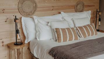 Een houten bed met witte en gestreepte kussens, een geweven hoofdbord en een bedlamp op een nachtkastje van hout.