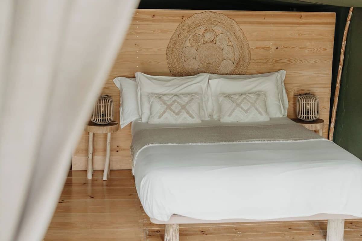 Un lit avec une tête de lit en bois, une literie blanche et deux tables de chevet ornées de lampes décoratives.