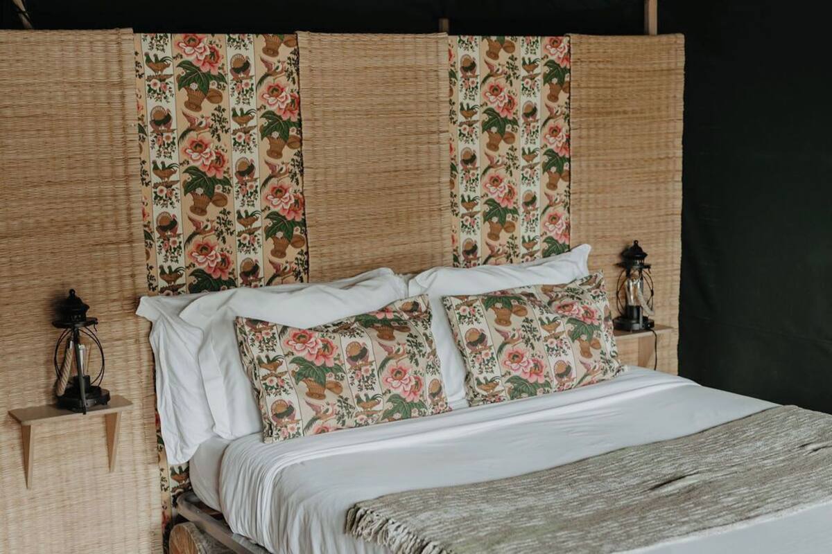 Un lit agrémenté d’oreillers à motifs floraux et recouvert d’une couvre-lit blanche, le tout mis en valeur par un mur en fibres tressées et un dais vert.