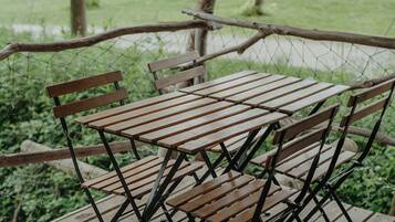 Eine Holzterrasse mit Metallgestellen für Tische und Stühle, umgeben von einem Drahtzaun und Bäumen.