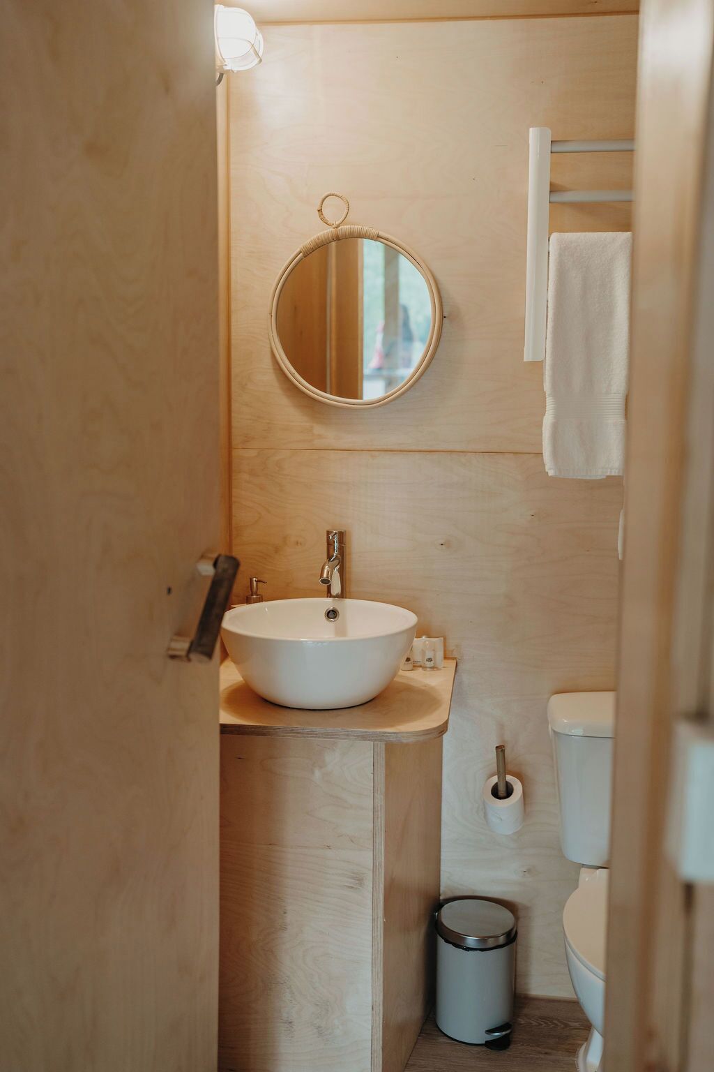 Ein kleines Badezimmer mit rundem Spiegel, Waschbecken, Toilette und Mülleimer.