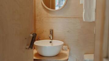 Ein kleines Badezimmer mit rundem Spiegel, Waschbecken, Toilette und Mülleimer.