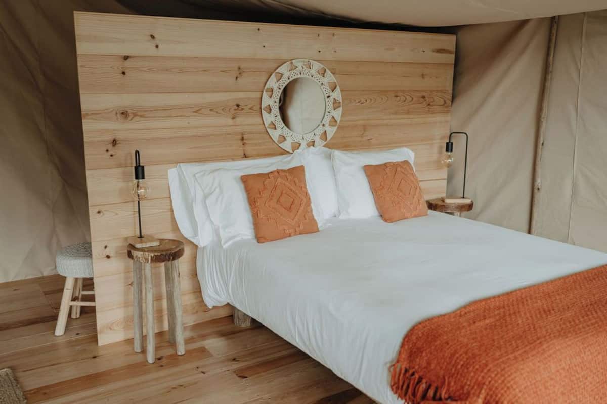 Une chambre confortable avec une tête de lit en bois, un miroir rond, une lampe de chevet et un petit tabouret.