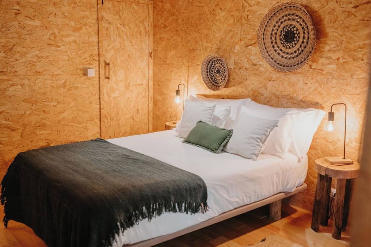 Une chambre à coucher aux murs lambrés, avec un lit, des oreillers et une lampe fixée au mur.