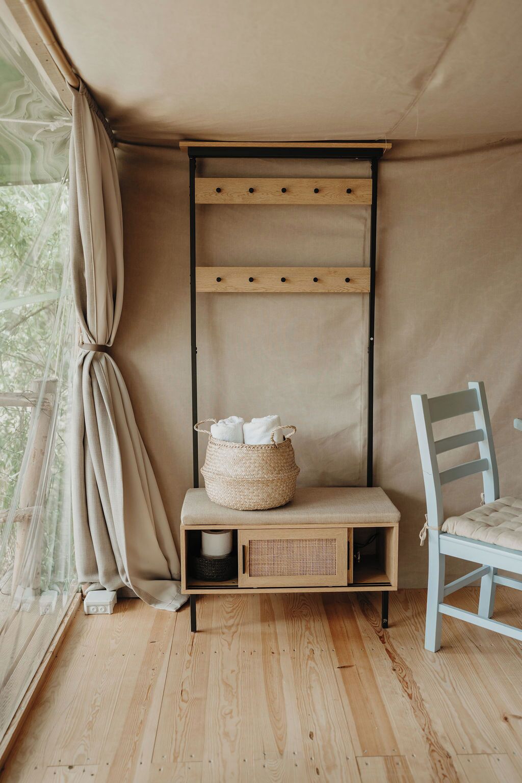 A tented room with a bench, a chair, and a woven basket with towels.