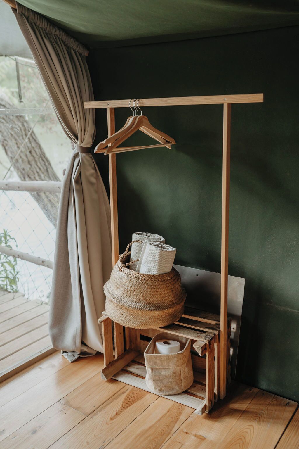 A wooden hanger rack with a rolled-up towel and a woven basket on a wooden shelf.