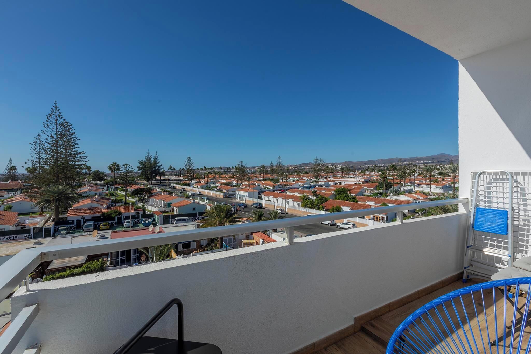 Un balcone con vista su una zona residenziale, una sedia blu e un muro bianco con un cartello blu.