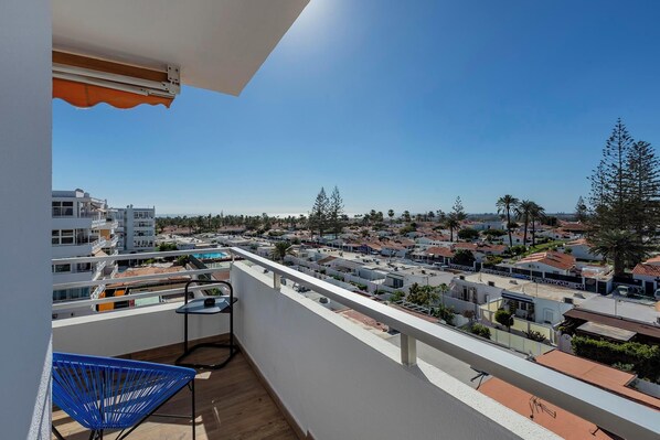 Un balcón con vista a una zona residencial, una silla azul y una pequeña mesa.
