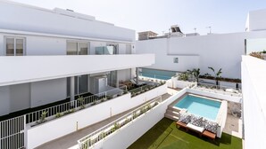 A modern building with a rooftop pool, multiple balconies, and a green lawn area.