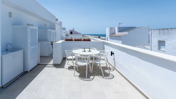 A rooftop terrace with a white table and chairs, a small sink, and a view of the sea.