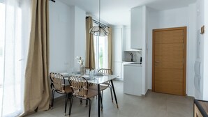 A modern kitchen with white cabinets, a wooden door, and a dining area with a glass table and wicker chairs.