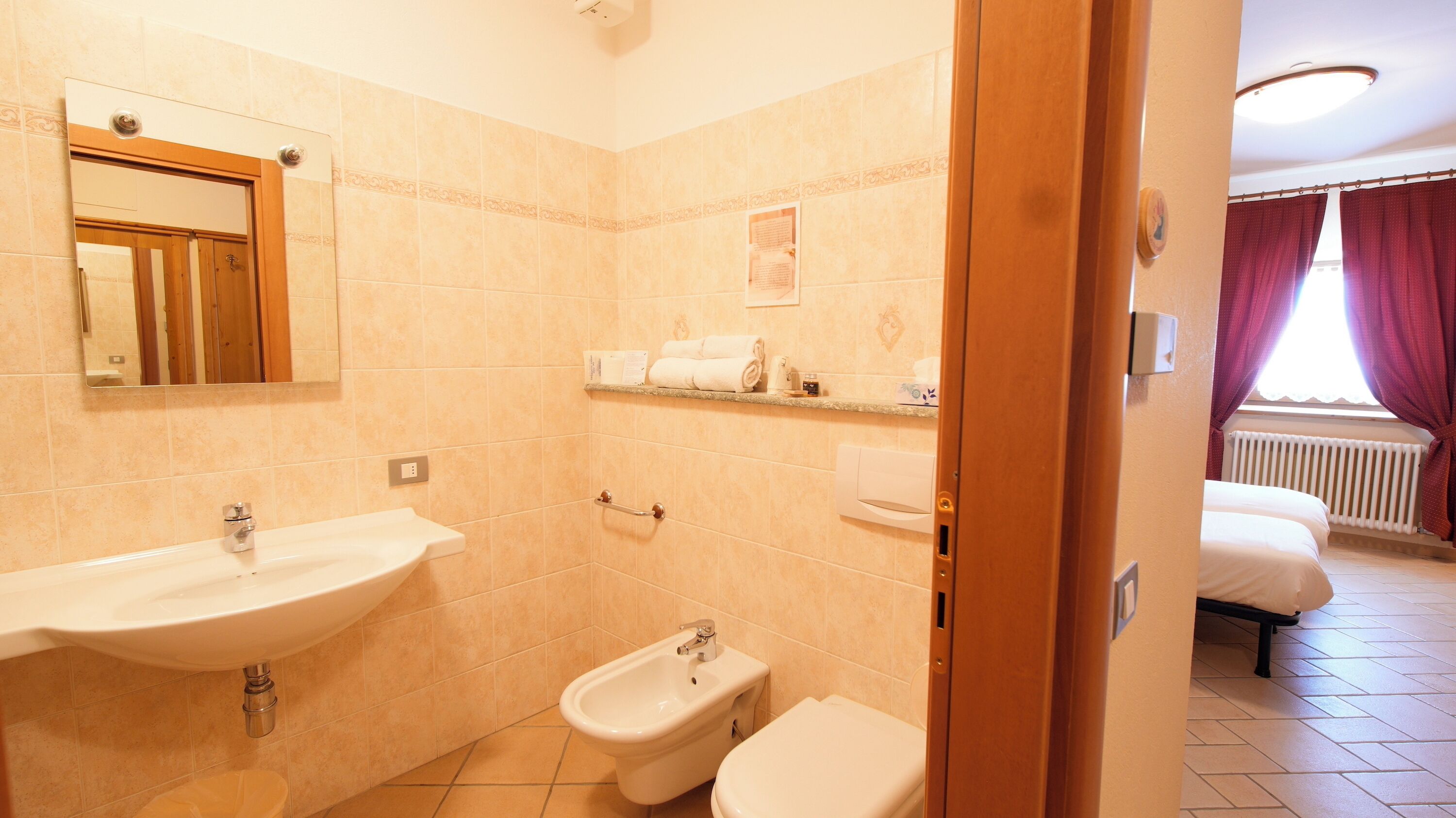 A bathroom with a sink, bidet, and toilet. There is a mirror above the sink, and a shower area is visible in the background.