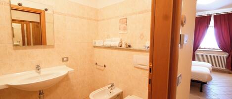 A bathroom with a sink, bidet, and toilet. There is a mirror above the sink, and a shower area is visible in the background.