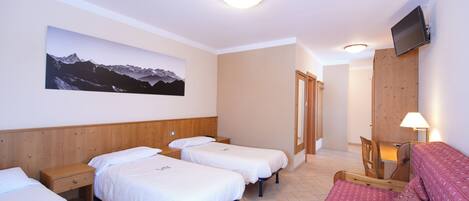 Ein Hotelzimmer mit drei Einzelbetten, einem hölzernen Kopfteil, einem angebrachten Fernseher und einem großen Gemälde von einer Berglandschaft an der Wand.