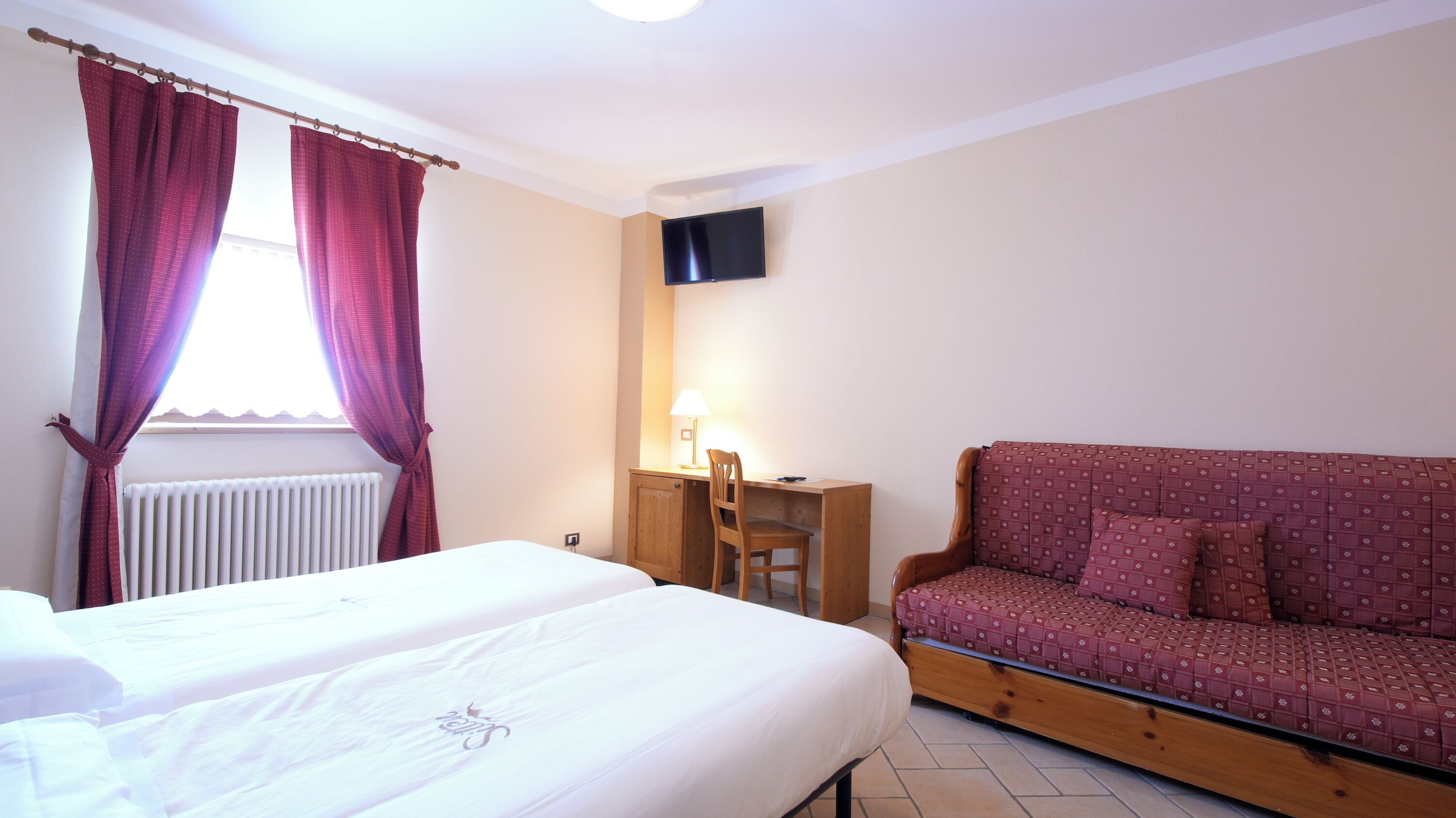 A bedroom with two beds, a desk with a chair, a television, and a sofa.