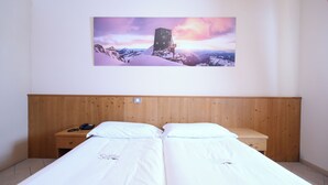Una cama doble con ropa de cama blanca, un cabecero de madera, una mesita de noche con un teléfono y una lámpara de pared.