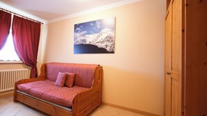 Una habitación acogedora con un sofá de madera, un radiador, una ventana con cortinas y un cuadro de una montaña en la pared.